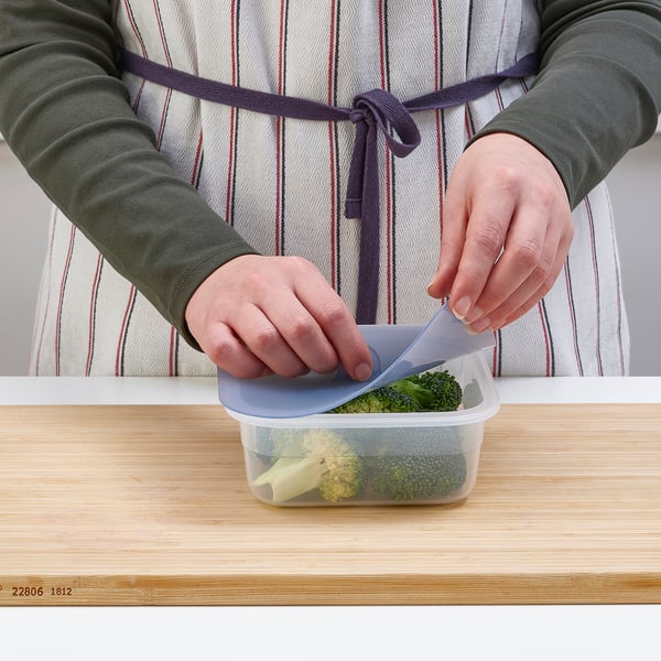 A person is closing a transparent container with broccoli. The lid seals to keep food fresh.