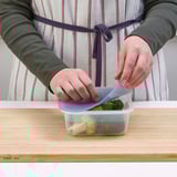 A person is closing a transparent container with broccoli. The lid seals to keep food fresh.