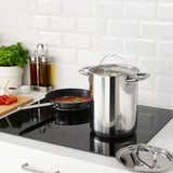 Modern kitchen with stainless steel pots and pans on black cooktop, cooking veggies and herbs. IKEA 365+ cookware.