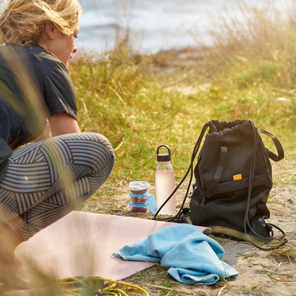 Woman sitting outdoors with a reusable water bottle, a backpack, and some snacks. The bottle has a strap for easy carrying.