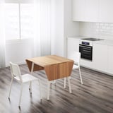 Modern white kitchen an IKEA PS 2012 bamboo drop-leaf table with two stacking white chairs, creating space-saving dining.