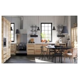 Modern kitchen with wooden cabinets, steel appliances, and wicker-seat table. White backsplash, large window.