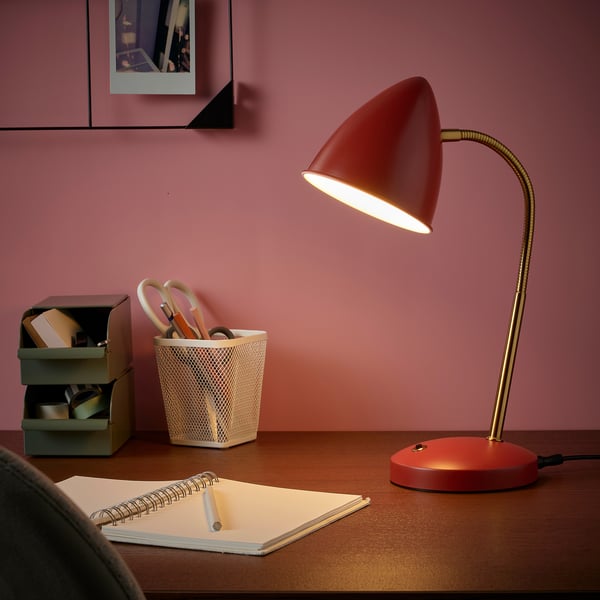 Red ISNÅLEN lamp with gold base, flexible neck, on desk beside notebook.