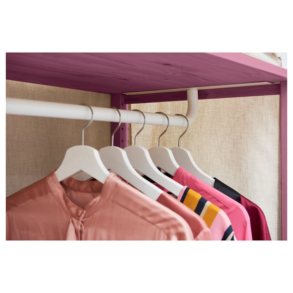 IVAR clothes rail holds shirts in pink and red tones. Steel hangers hook into a white rail, all set against beige fabric.