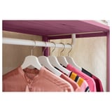 IVAR clothes rail holds shirts in pink and red tones. Steel hangers hook into a white rail, all set against beige fabric.
