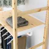 Wooden shelf with foldable hanger, holding folded grey sweater. Part of IVAR storage system.