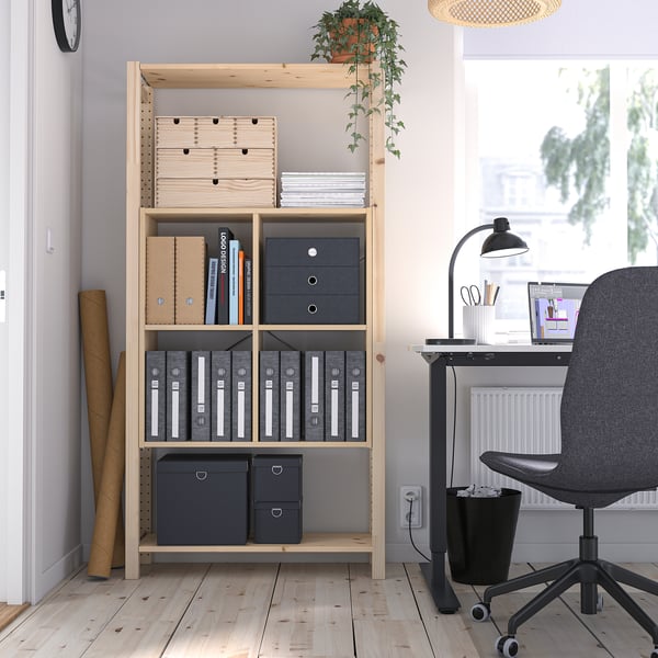 IVAR bookshelf with grey boxes, holding books & files, beside desk & window.