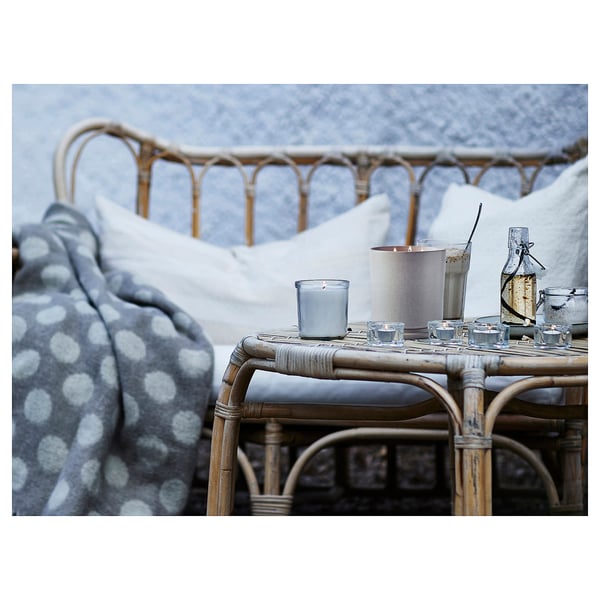 Cozy outdoor set-up: wicker furniture with blue polka dot blanket, candle, and glassware.