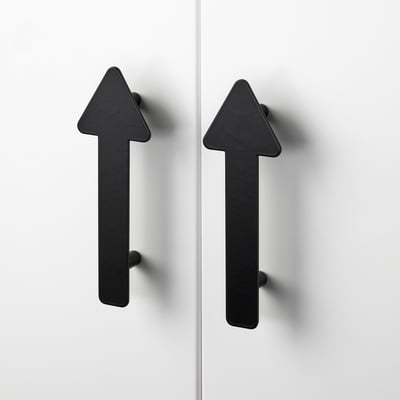 Two modern, minimalist black arrow-shaped handles attached to white cabinet doors. High-quality, sleek finish with robust design.