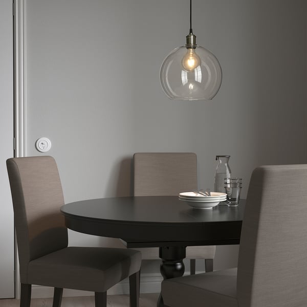 JAKOBSBYN pendant lamp above dark dining table with grey chairs, emitting warm light.