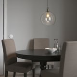 JAKOBSBYN pendant lamp above dark dining table with grey chairs, emitting warm light.