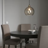 JAKOBSBYN smoked glass pendant light over small black dining table with grey chairs, warmly illuminating the cozy setup.