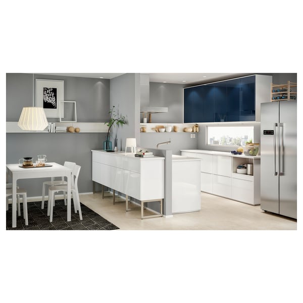 Modern kitchen with white furniture, including a dining table and chairs, fridge, and decorative items. Grey walls and dark blue cabinets.
