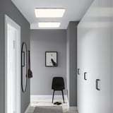 Modern hallway with gray walls, slim light panel, black chair, shoe rack, round mirror, and small rug.