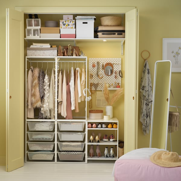 Organized closet with white JONAXEL storage, clothing hangers, shelves, and decor items; yellow walls.
