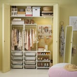 Organized closet with white JONAXEL storage, clothing hangers, shelves, and decor items; yellow walls.