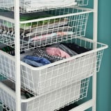 A white JONAXEL storage unit with multiple wire baskets holding folded clothes. Each basket is rectangular and stacked vertically.