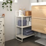 White metal storage shelf with towels and toiletries between vanity and wall.