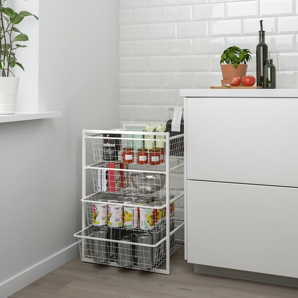 White JONAXEL storage rack with multiple wire baskets holding various items, placed beside a white cabinet in a modern kitchen.