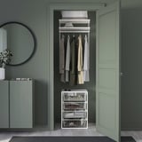 Open closet with JONAXEL white metal storage, clothes, green walls, light wood floors, mirror, cabinet.