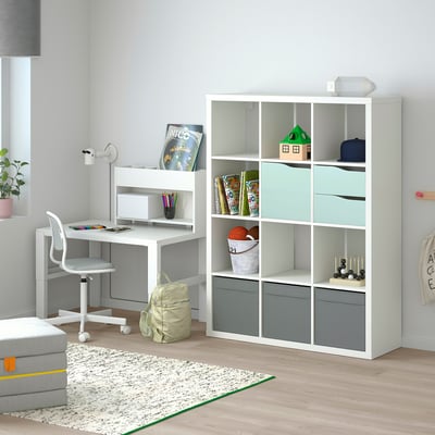 Modern kids study setup with KALLAX shelving unit featuring door inserts, holding books, toys, and desk with chair.