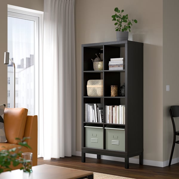 KALLAX black bookshelf with green bins, taller than chair, airy design.