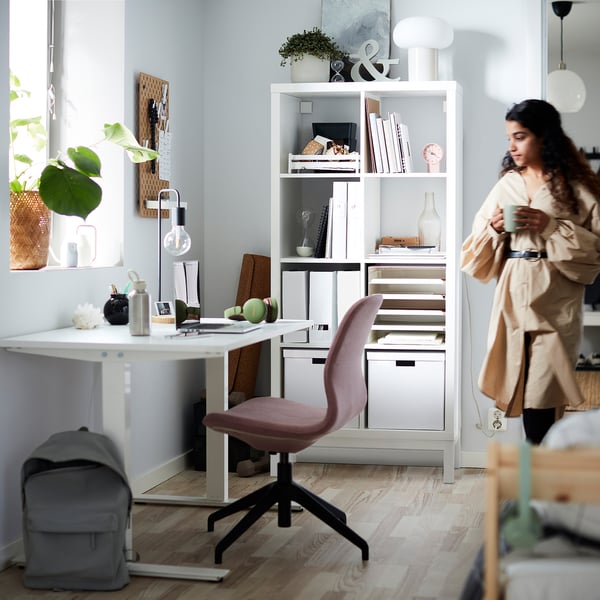 Woman with cup by KALLAX shelves and desk setup.