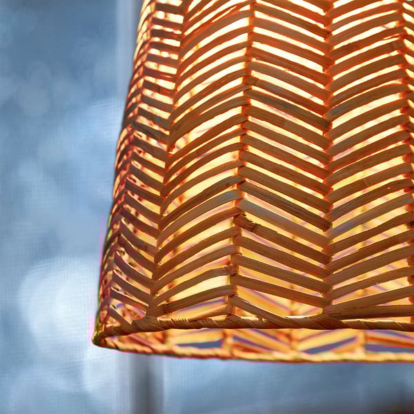 Close-up of intricately woven rattan pendant lamp shade, emitting warm light. Herringbone pattern is visible, highlighting craftsmanship.
