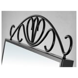 Black wrought iron mirror with ornate scrollwork detail at the top against a gray wall.