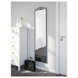Mirror on grey wall beside dresser, handbag on floor, reflects windowed room.