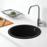 Black sink with quartz countertop, chrome faucet, knife, colander with broccoli.