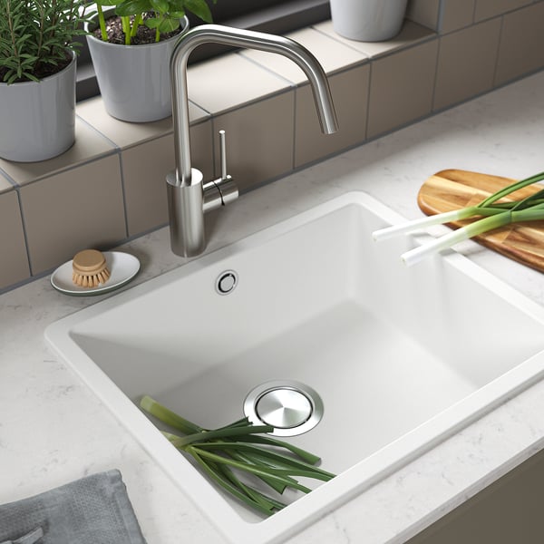 Modern kitchen sink with stainless faucet, green onions, quartz countertop, and accessories.