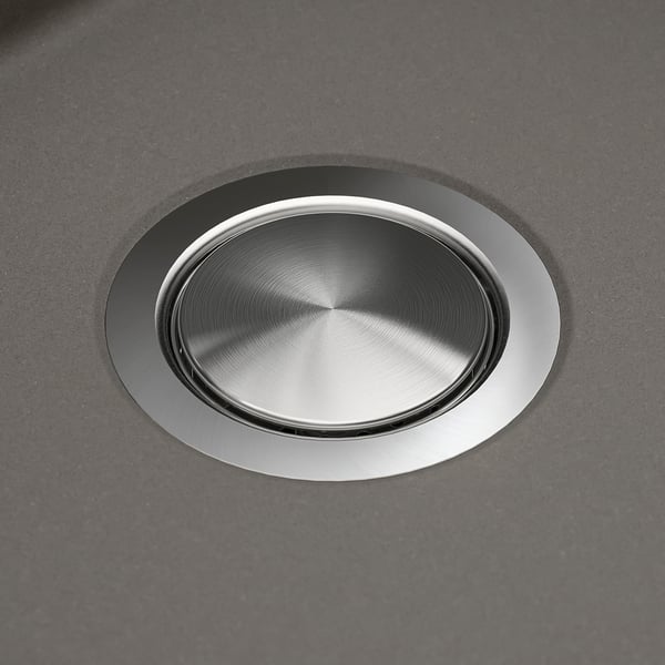 Stainless steel sink drain cover, smoothly integrated into a dark quartz countertop, showcasing durability and seamless design.