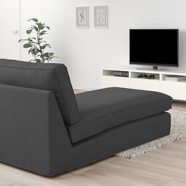 Modern living room with dark gray KIVIK sectional sofa, wooden floor, white tv stand, and wall art. Sofa appears large compared to other items.