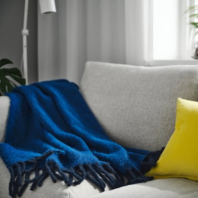 KLIPPOXEL blue throw on sofa, large, soft, fringed ends, with yellow pillow.