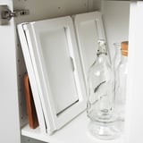 Foldable bed tray stored vertically against cabinet wall with kitchen items nearby.