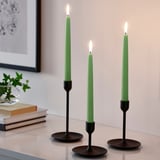 Three green candles in black holders between books & frame.