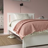 Cozy bedroom with pinkish-beige KLOTSTARR blanket, waffled texture, matching cushion, slippers, rug, and plant.