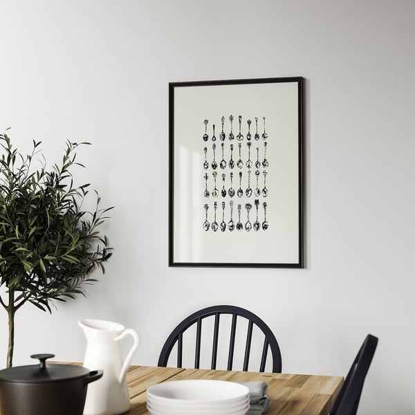 Black-and-white abstract art on gray wall over dining table with plant and dishes.