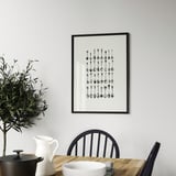 Black-and-white abstract art on gray wall over dining table with plant and dishes.