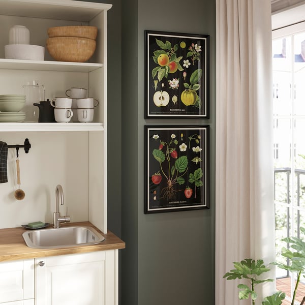 KNOPPÄNG prints with fruit art hang above kitchen sink, adding vibrant color to dark green wall.