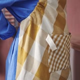 Apron with large checkered squares, pocket, and adjustable strap. Perfect for cooking, with a hanging loop.