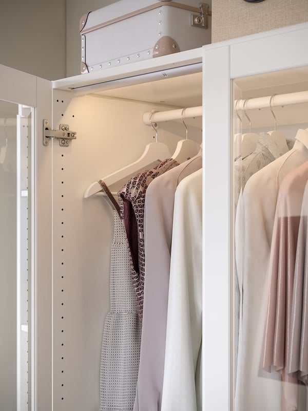 KOMPLEMENT white hanging rail, made of steel, holding light-colored clothes with hangers in a wardrobe.