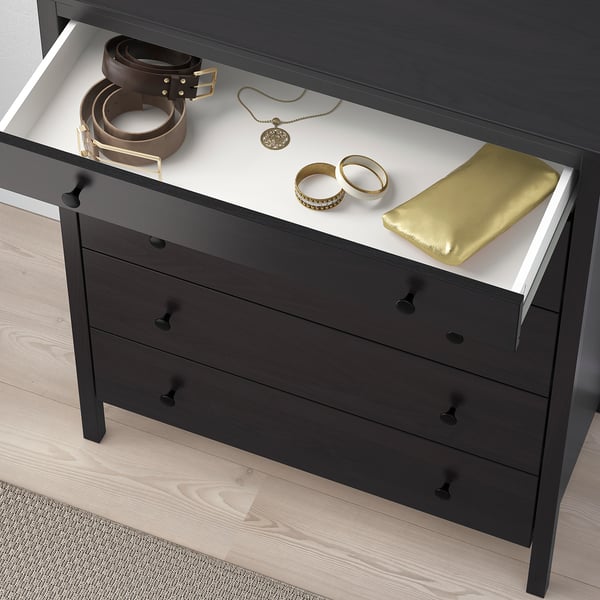 Black dresser with 3 drawers, one open. Belts, jewelry, gold pouch inside. Bedroom storage.