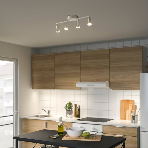 Modern kitchen with ceiling lights, wooden cabinets, steel appliances, black island with bowl, cutting board, and olive oil.