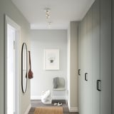 Modern entryway with ceiling light, illuminating gray chair & brown bag on wall hook. Tall closet on right, white door on left.