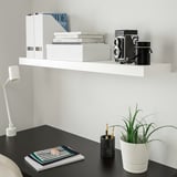 White LACK shelf with books & camera above dark table & lamp.