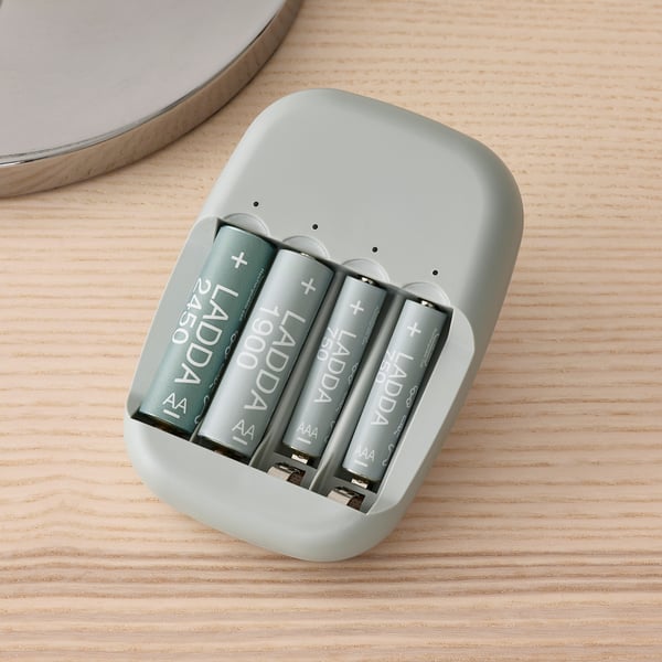 Four gray LADDA rechargeable batteries sit in a light green charger on a light wood surface.