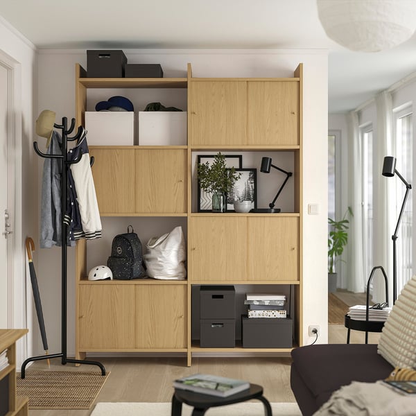 Wooden storage unit with open and closed shelves, housing various items, installed next to a black coat stand and near a dark brown couch.