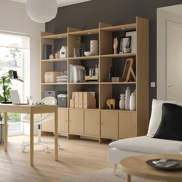 A light wooden LÅDMAKARE storage system against a dark wall. It open shelves and cabinet doors, displaying decor items and books.